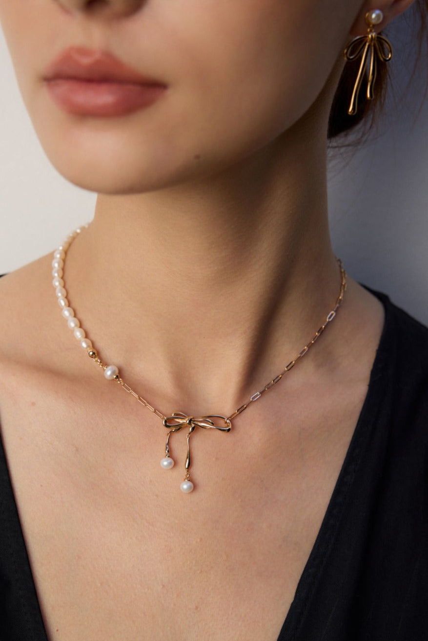 Close-up of a woman wearing a delicate necklace with a bow and pearl accents.